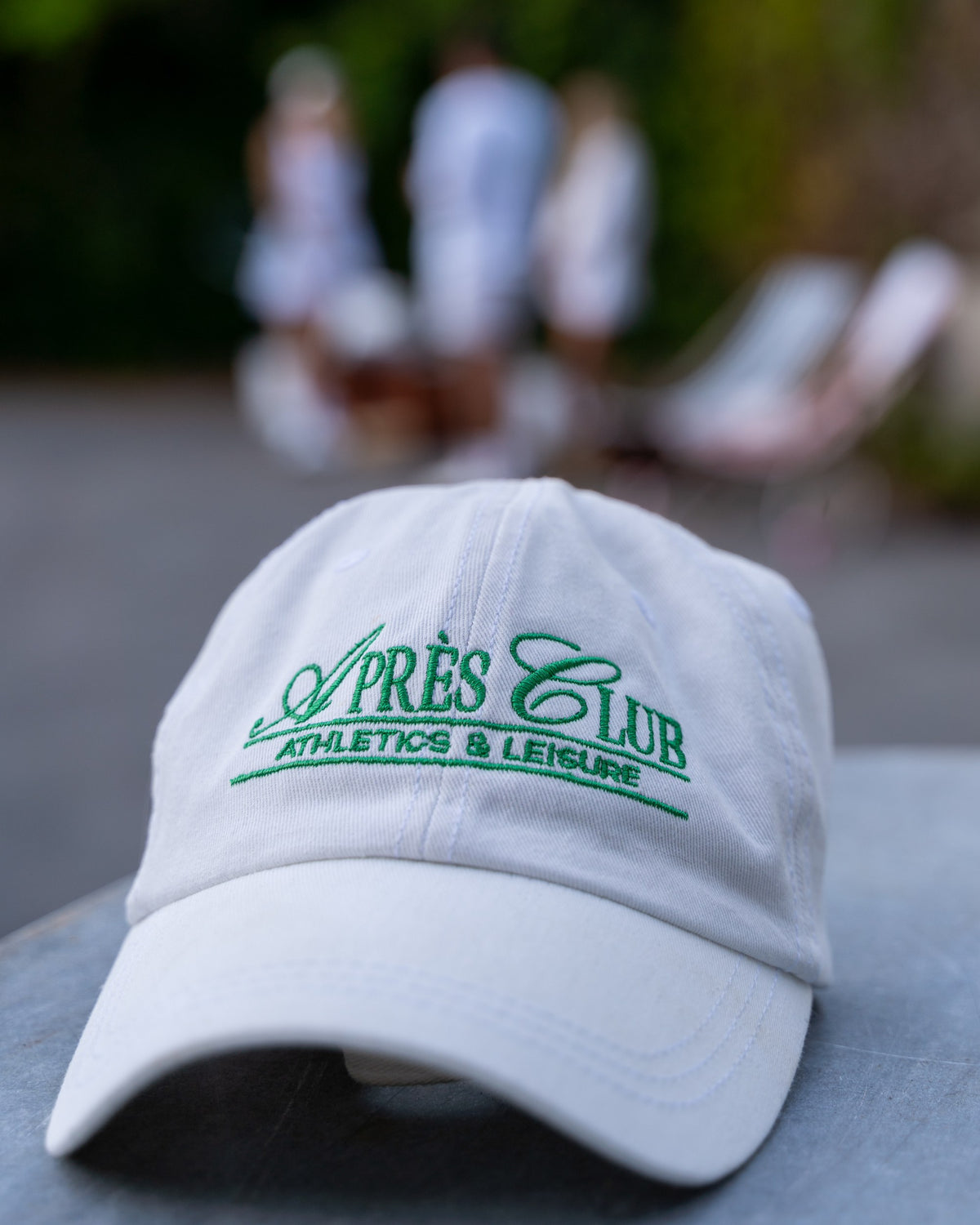White Après Club cap with green embroidery on a tennis court, styled photo